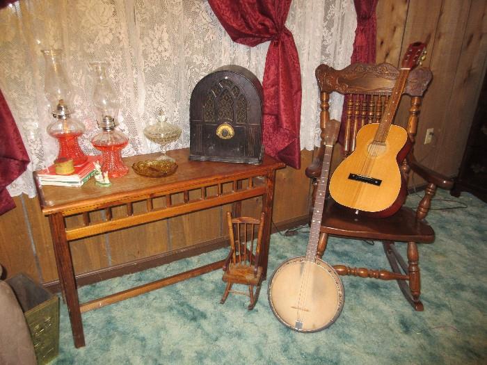 Shaker style table, kerosene lamps, electrified radio (works), banjo, guitar, wooden rocking chair.