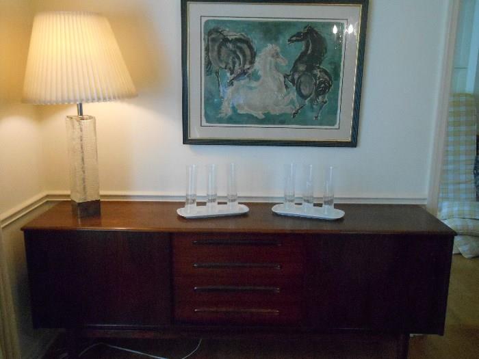 Dining Room:  HOUSE OF DENMARK sideboard/credenza is 6' 4" wide x 31" tall x 17-l/2" deep.  It has a sliding door on each side and four shallow drawers in the middle.  The glass lamp on the left is Finnish, and the modern lithograph is signed and numbered (74/95) by Swedish artist HANS ERNI (measures 36" wide x 29" tall).