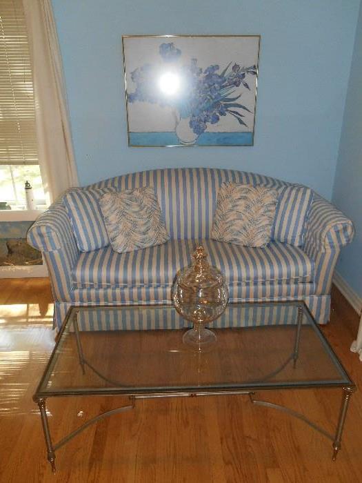 Bedroom #2:  A cream/blue striped 76" sofa sleeper; a glass top silver/gold metal table measures 48" x 23"; a floral print; and a glass jar.