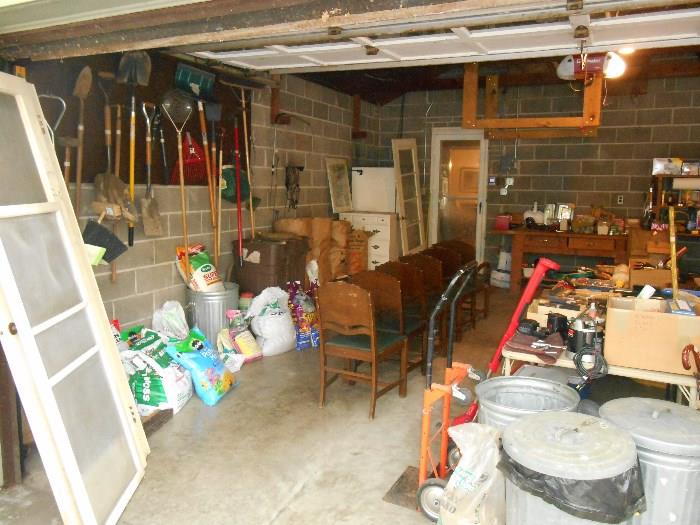 Garage:  A view of the garage looking toward the inside door.  To the left are a few vintage wood screen doors, a selection of yard tools, and numerous bags of grass seed, bird seed and more!. 