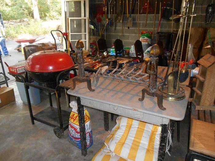 Garage:  A grill+stand; vintage kitchen table with one drawer; fireplace grate; fireplace tools; andirons.  Four yellow/white striped chair cushion and one chaise cushion are under the table.
