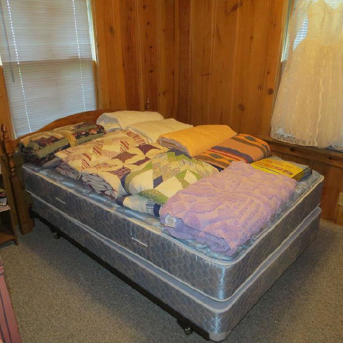 Double bed with unused mattress and box springs and headboard; quilts and bedding.