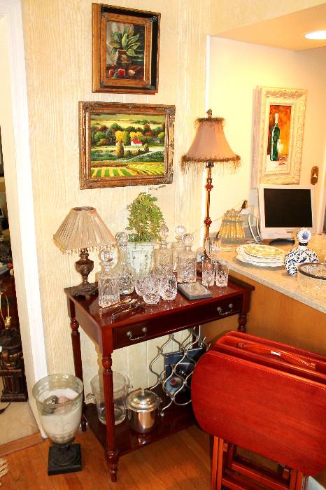 Side table with crystal decanters, barware, lamps, and several original paintings