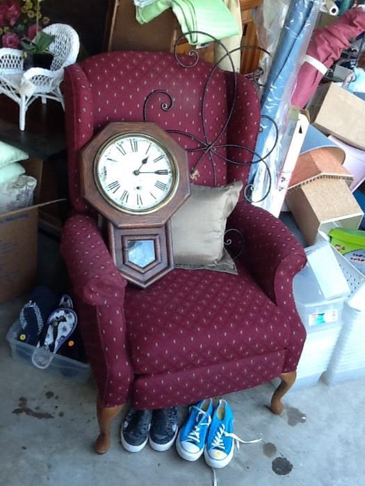 Upholstered wingback chair, vintage wall clock, ornamental cross.