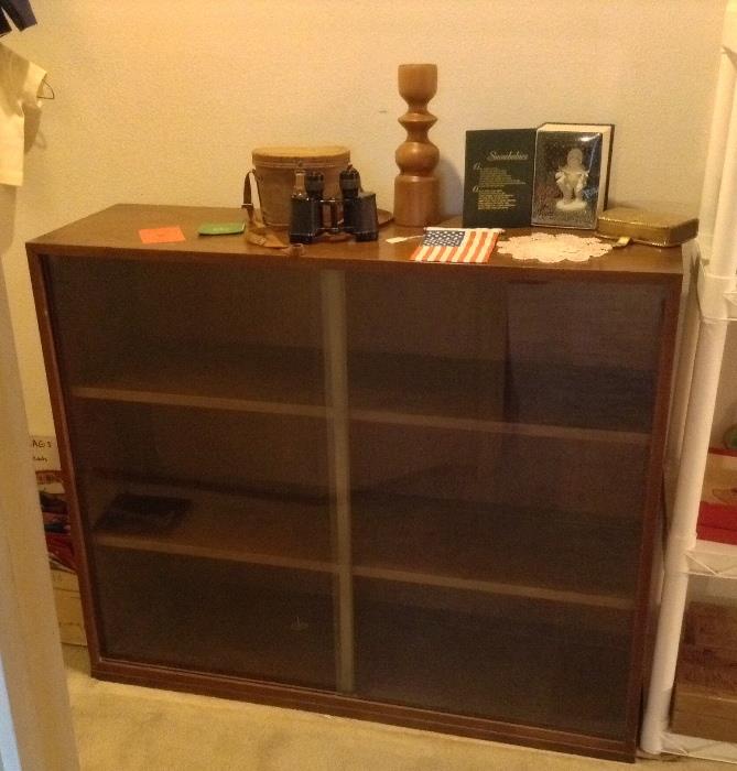 Wooden display cabinet (bookcase) with sliding glass doors. Measures 44" long, 37" high & 14" deep.  Interior shelves are fixed (i.e. not adjustable). On top: vintage binoculars with leather case, mod wood candle holder, Dept. 56 skating snow baby in original box
