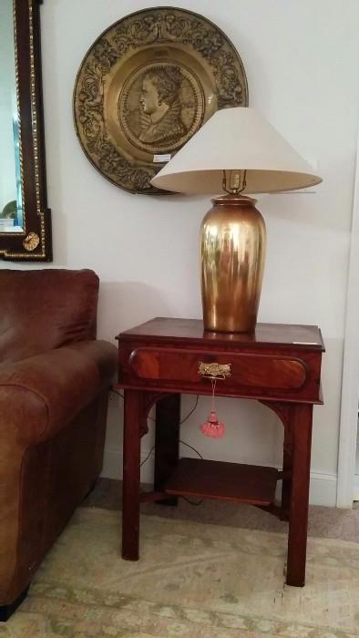 Antique mahogany 1-drawer side table, with one of a pair of gold porcelain table lamps, one of a pair of antique English brass chargers as wall hangings