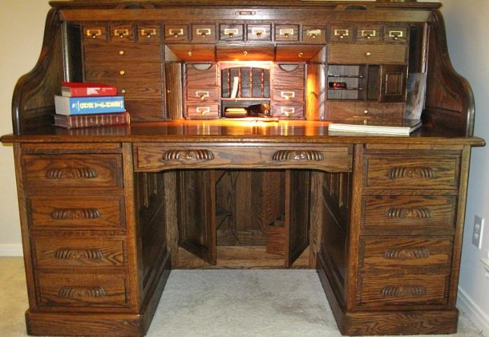 Oak Roll Top Desk shown open, center upper drawer pulls out to light surface. 12 pigeon hole  drawers with tab pulls brass label holders.  Many other drawer and compartment. Files drawers on each side below 2 drawers.  Underneath desk is a hidden bar compartment.