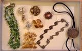 More jewelry including green Austrian crystal necklace, rhinestone pin by Kramer, pink & purple Coro pin, other signed pins, Danecraft sterling necklace, gold bird pin by Alva Studios (museum reproduction), bolo tie with 1889 Morgan silver dollar