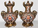 LOT#62  CHINESE PORCELAIN AND BRONZE COVERED URNS WITH STANDS, C 1900, PAIR, H 16", both having small porcelain lids with pine cone finials. Long narrow neck with bulbous body. Adorned with bronze mounts and bronze stands.