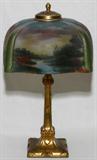 LOT#1021  REVERSE PAINTED GLASS & GILT METAL TABLE LAMP, ATTRIBUTED TO PITTSBURGH LAMP CO., C. 1920, H 20", Squared shade painted at the interior with a river setting.  No apparent markings.  Shade W.11 1/2".