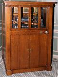 LOT#2051  MILLS NOVELTY CO. SINGLE VIOLANO VIRTOSO, CIRCA 1907, H 63", W 43", Plays 1-15 nickels, in an oak case, the lower cabinet with two hinged doors which open to the paper roll rack; includes a violin, piano keys.  The upper section is inset with four beveled glass panels. Provenance: Mike Gorski.