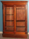LOT#2149  LATE VICTORIAN WALNUT BOOKCASE, C. 1900, H 70", Two doors inset with glass panels, overhanging stepped cornice, fitted with wood shelves.