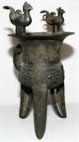 Lot# 1077 CHINESE BRONZE WINE VESSEL (JUE), H 17", W 9 1/2", Cast with two birds perched on the flaring rim, a band of taotie-like motifs about, with a single handle, raised on three blade-shaped supports. From the Collection of John P. O'Hara, Bloomfield Hills, Mich.