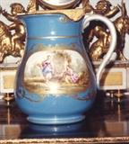 272/251  Pitcher.  A 20th century French porcelain Sevres style pitcher of bulbous form showing two hand painted oval reserves within a gilded outline on a light blue ground.  One side shows two maidens.  The other displays a man seated at a well with a young girl nearby.  The embellished handle is in white.  Unsigned.
Marked, on the bottom with incised marks and the number 872 within an oval in underglaze blue.
8" high.  $275.00
