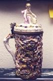 168/229  Stein.  An early 20th century Italian Capodimonte stein with an eagle thumb lift, the lid with a finial of a full form putto holding a cornucopia.  The sides are thickly decorated, in relief, showing a farm scene.
12" high.  $1200.00