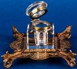 Lot #73, Vintage Art Deco Tiffany Studios Brass Inkwell
A nice little Art Deco style inkwell with bronze / brass base and heavy glass insert ink jar. The base has four feet which have been riveted into place and it is decorated with intricate carvings of both floral and geometric designs. An oval plate affixed on the bottom reads "Tiffany Studios, Broadway, NY". The ink jar has beveled glass on all edges and a hinged lid. The metal mount that secures the lid to the jar is loose and the glass has a chip in one bottom corner. Still displays beautifully. Measures 3" tall x 4.75" x 4.75". Tag Words: Intdes, desktop, school, desk, home office