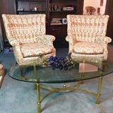 Pair 1950s channel-back chairs in gold and white behind brass and glass coffee table topped with blue retro grape cluster.