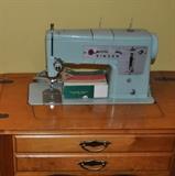Singer aqua/turquoise Model 338 sewing machine in cabinet with instruction manual and accessories.