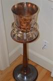 An Art Deco-inspired silver-plate wine bucket by Christofle on a silvered-plate and mahogany stand. The bucket's handles are enameled. It is very difficult to find a Christofle bucket with the stand. The stand alone stands 24-1/2" high, and the base is 11-1/2" in diameter. The bucket is 8-1/4" high and 7-3/8" in diameter.