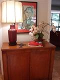 One of a pair of credenzas with sleek modern lines, and one of a pair of oxblood color ceramic lamps.