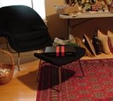 Black fabric womb chair and foot rest, Bokhara rug in deep crimson instead of the usual bright red background.