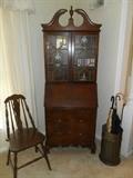 Living Room:  A classic secretary/hutch has a bonnet top with finials, glass doors, slant front, and three serpentine drawers.   It measures  77" tall x 28" wide x 16" deep.  We displayed books, vases and figures in this one.  To the  left is an antique splat/tapered back Windsor chair.  To the right is a brass umbrella stand with umbrellas.
