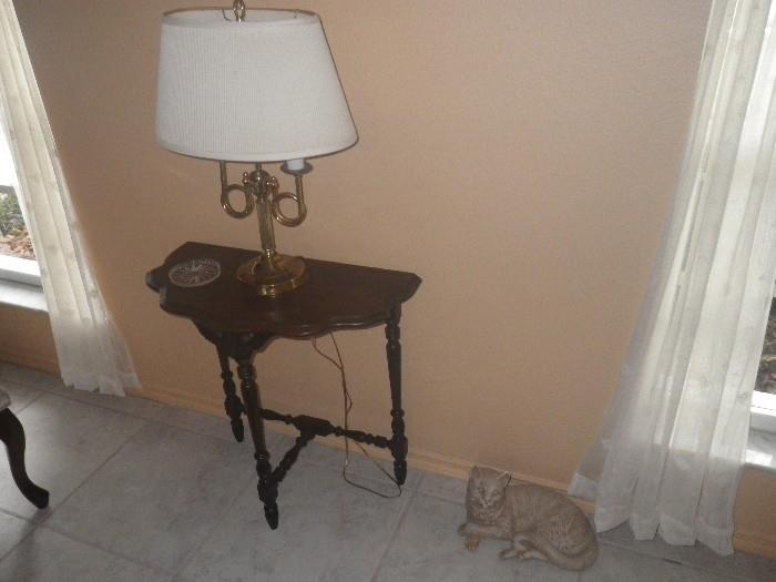 Antique side table and a brass lamp. Also, cat sculpture on the floor.