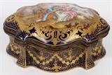 Lot#1023, FRENCH SEVRES STYLE PORCELAIN DRESSER BOX, SIGNED, H 3", L 6 1/2"Cartouche shape with hinged cover centered by a hand painted 18th century courting scene, signed at the lower right, possibly Lauput, cobalt blue ground with fired gold lattice, scroll and swag motifs. Mark of interlaced "L's" under glaze with "D" date mark (see additional photo). Measures H.3" x 6 1/2" x 4 1/4".