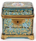 Lot#1031, MOSER ENAMELED GLASS JEWELRY BOX, LATE 19TH C., H 3 1/2", W 3 1/2"Decorated over an azure colored glass with gilt enameled leaf, vine and flower motif.  Having a central vignette of a putto at the top and brass mountings.  Measuring H.3 1/2" x 3 1/2" x 2 1/2".