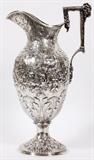Lot#1143, S. KIRK & SON SILVER EWER, BALTIMORE, C. 1846-1861, H 17"Classic urn-form coin silver ewer with an angular handle surmounted by a ram's mask, decorated allover with repousse flowers and acanthus leaves framing two architectural vignettes; stamped underneath "S. Kirk & Son, 11 oz." (see additional photo).  Measures H.17" to the top of the handle, W.9" overall.  Weighs approximately 38.45 troy oz.