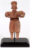 Lot#337, PRE-COLUMBIAN, TERRACOTTA FIGURE, H 6 1/2"A figure holding a dog. Mounted on a black painted base with bent wire support. DuMouchelles does not guarantee the age of this article. Please preview in person and make determination.