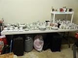 Garage:  large table loaded with painted mugs, coffe cups, plates sets of glass items, suitcases