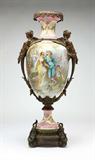 Lot# 1110 A monumental gilt bronze-mounted Sevres style porcelain pink-ground urn 









Probably late 19th / early 20th century, signed 'Bertren', the scalloped anthemia-decorated rim suspending tassels, above a tapering neck and oviform body decorated to one side with a courting couple and cherubs and to the other with figures playing blind man's bluff, flanked with winged female term handles, over a spreading socle on a reeded circular base with laurel wreath loops, overall. 46'' H x 22'' Dia. est:$3000/5000