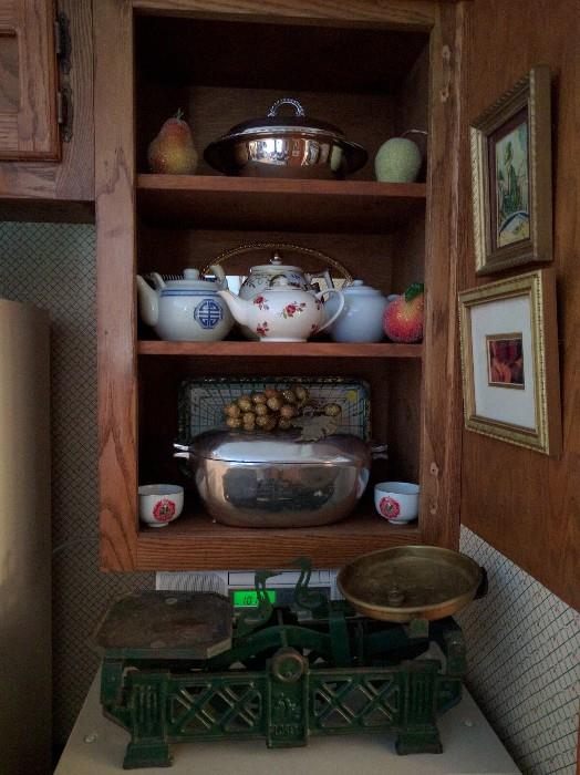 The kitchen is overflowing with all sorts of collectible treasures, from sets of glassware, teapots, cooking utensils, pots, pans, sets of china, you name it!                    Sitting on the counter is a cool antique metal scale.