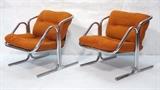 Lot 278:  Pr Jerry Johnson Chrome Tubular Lounge Chairs. Unique form frame. Orange Fabric Cushions. Black sling support: Dimensions:  H: 27 inches: W: 25.5 inches: D: 30 inches --- 