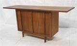 Lot 512:  American Modern Walnut Credenza. Small Center Cabinet with long extended banded top. Brass piano hinges. Two doors. : Dimensions:  H: 32 inches: W: 71.25 inches: D: 21.5 inches --- 