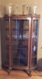 Antique oak display cabinet with curved glass - made by the Northwestern Cabinet Co. of Burlington, Iowa. (37" wide & 62" tall). With glass candleholders & hurricane lamps on top.