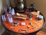 Knick knacks on table: glass shoes, crystal salt & pepper set, "purpled" glass inkwell, old leather bound books, brass bird clip, old keys, brass candle snuffer, old eyeglasses, figural match holder (girl with basket), wooden boxes, brass postal scale, art piece with bird on binoculars, tiny frame