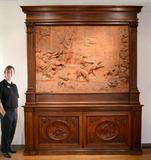 Lot 101: MONUMENTAL CARVED WOOD FRESCO/CREDENZA ''THE HUNT OF DIANA'': The large wood carved historismus fresco depicts the 17th century painting by Domenichino (Domenico Zampieri) titled ''The Hunt of Diana'' painted in 1617-1618 for Cardinal Aldobrandini. Purchased in Piacenza, Italy. The family was using the top half as a pedestaled headboard (pedestal included) and the double door base as the footboard making a strikingly impressive king-size bed surround. The base is inset with deeply carved oval panels, the left depicting attacking hounds, the right depicting Eros, a scantily clad semi-nude woman and her love struck suitor. 122''h x 14''d overall. Top measures 81''h x 10''d, bottom measures 41''h x 14''d. It measures 102 1/2'' at its widest point at the crest.
