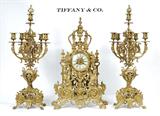 Lot 1001:  TIFFANY & CO. LOUIS XIV STYLE GILT BRONZE CLOCK GARNITURE SET: A fantastic clock garniture set by Tiffany & Co. to include gilt bronze mantle clock with applied decoration to include urn, griffon, Bacchus, masqueron, foliate and architectural motifs. Porcelain dial with Roman numerals marked Tiffany & Co., New York. Time and strike movement marked Tiffany & Compe, New-York. Serial number 3977, pendulum and back bezel with matching numbers. 25 1/4'' h. x 16 1/4'' x 6 1/2''. Sold with matching 6 light candelabra garniture set, marked 132 inside base. Measures 28 1/2'' h. x 11 1/2'' dia. Est. $6000/8000**
CONDITION: Currently running however not guaranteed to continue. Key and pendulum in office.
