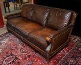 Lot 1227:  WHITTEMORE SHERRILL BROWN LEATHER SOFA: Supple brown leather tacked to carved wood frame with applied decoration. Removable seat cushions. Overall 34'' h. x 80'' x 40''.