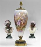 Lot 1004:  PAIR CONTINENTAL MAJOLICA BLACKAMOOR BUSTS: Porcelain bust of man and woman, each finely decorated. Man with impressed 499 and underglaze 88 on base, woman with impressed 500 over 3 on back. Man measures 13'' h. x 8''.Lot 1068:  SEVRES STYLE PORCELAIN LAMP SIGNED FUCHS: Large Sevres style porcelain body with hand painted scenes of cherub making arrows on one side, 3 cherubs with maiden verso. Signed L.? Fuchs. Mounted with cast metal, marble and brass base. Overall 30 1/4'' x 10 1/2'' dia.
CONDITION: Crazing throughout, staining at base of porcelain.