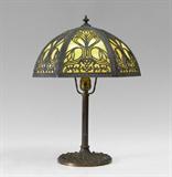 Lot 1047:  VINTAGE MILLER SLAG GLASS TABLE LAMP: Base stamped Miller 971 underneath, original Miller socket. 19'' h. to top of finial x 7 1/4''. 6 panel multi hued bent slag glass shade with filigree frame, 7'' h. x 14 1/4''.