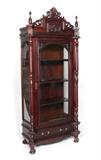 Lot 1280:  A GRAND CARVED MAHOGANY DISPLAY CABINET: 20th century in the Victorian style. Carved crest with 2 spire finals over glass door and sides, 2 turned full column supports. 3 interior shelves, lower drawer. On stylized claw and ball feet. 88 1/2'' h. x 40 1/4'' x 20 1/4''.