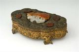 Lot 1347:  CHINESE EMBOSSED GILT METAL DRESSER BOX: Embossed gilt metal box with foo dogs motifs all over. Hinged lid with carved soapstone medallions, largest with food dogs motif as well. Stamped China on base. Overall 3'' h. x 9 1/2'' x 6''.
CONDITION: Loss of gilt to top of lid.