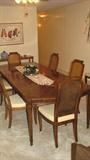 This handsome Tryon Manor by Drexel dining room set includes 8 side chairs (6 are pictured here) and could comfortably seat even more.  Displayed here with both of the 18-inch leaves installed, the beautiful finish on the table top features book-matched crotch-grained wood in a medium-dark stain.  The chairs have lovely tone-on-tone ivory upholstery on the cushions and cane-inset backs