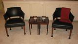 The two balck vinyl-upholstered chairs are roughly barrel-shaped with nail-head trim and casters to be able to move them around easily.  More than one of us sat in them while setting up the sale and noted that they are of sturdy construction but have clean lines and are remarkable comfortable to sit in.  In addition, the two delicate tables between them are cherry-colored finish with brass detail and do double duty.  The table tops are actually detachable trays.