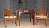 These two arm chairs appear to be teak and have large cane insets in the backs as well as casters for easy movement of the chairs.  The upholstery on the seats is a crem-colored Victorian-style floral.