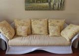 Sculpted rattan cream colored sofa with throw pillows.