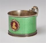 Russian Faberge Enameled Silver Cup
The side inset with a coin showing Catherine the Great, on green enameled ground. Marked underneath 2" high, 3 1/2" long across handle 3.7 ozt gross.  Bid at www.fairfieldauction.com today through Wed. July 20th
